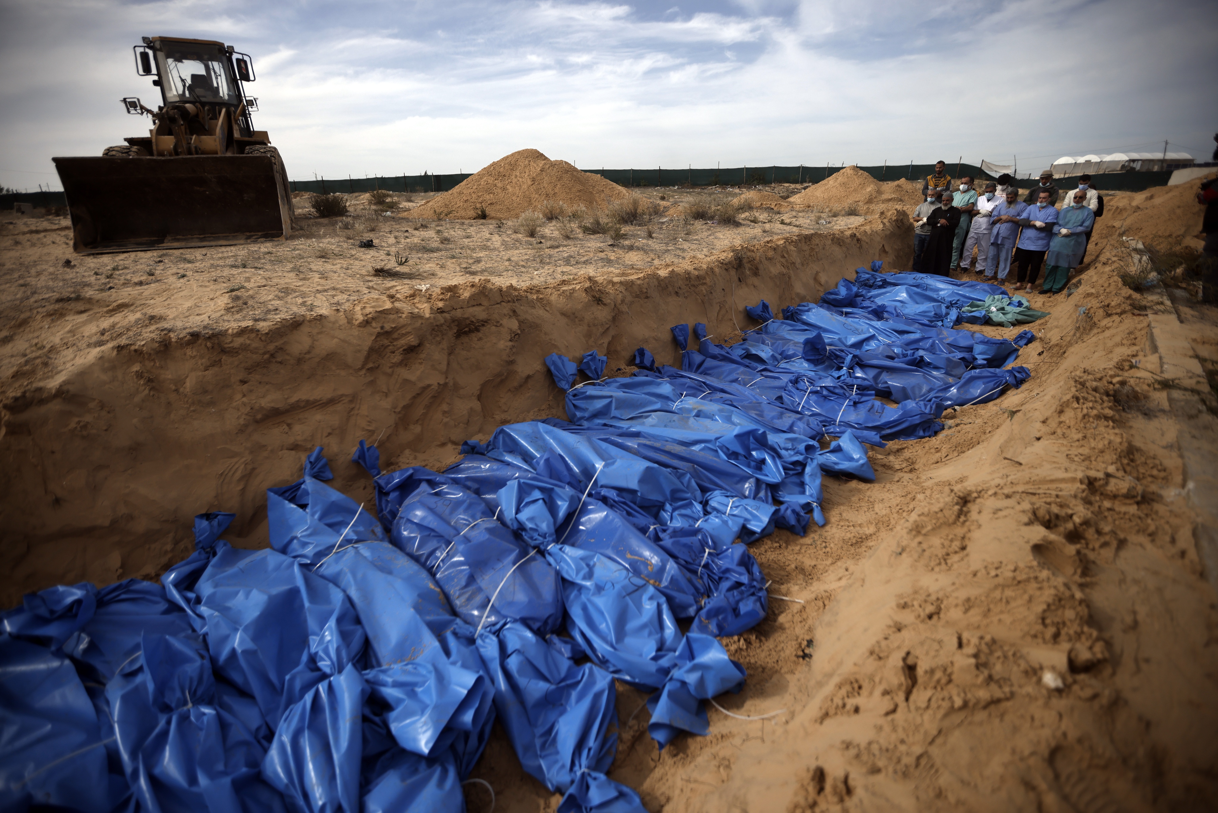 Palestinians pray over bodies of people killed in the Israeli bombardment who were brought from the al-Shifa Hospital before burying them in a mass grave in the town of Khan Younis, southern Gaza, on November 22, 2023.
